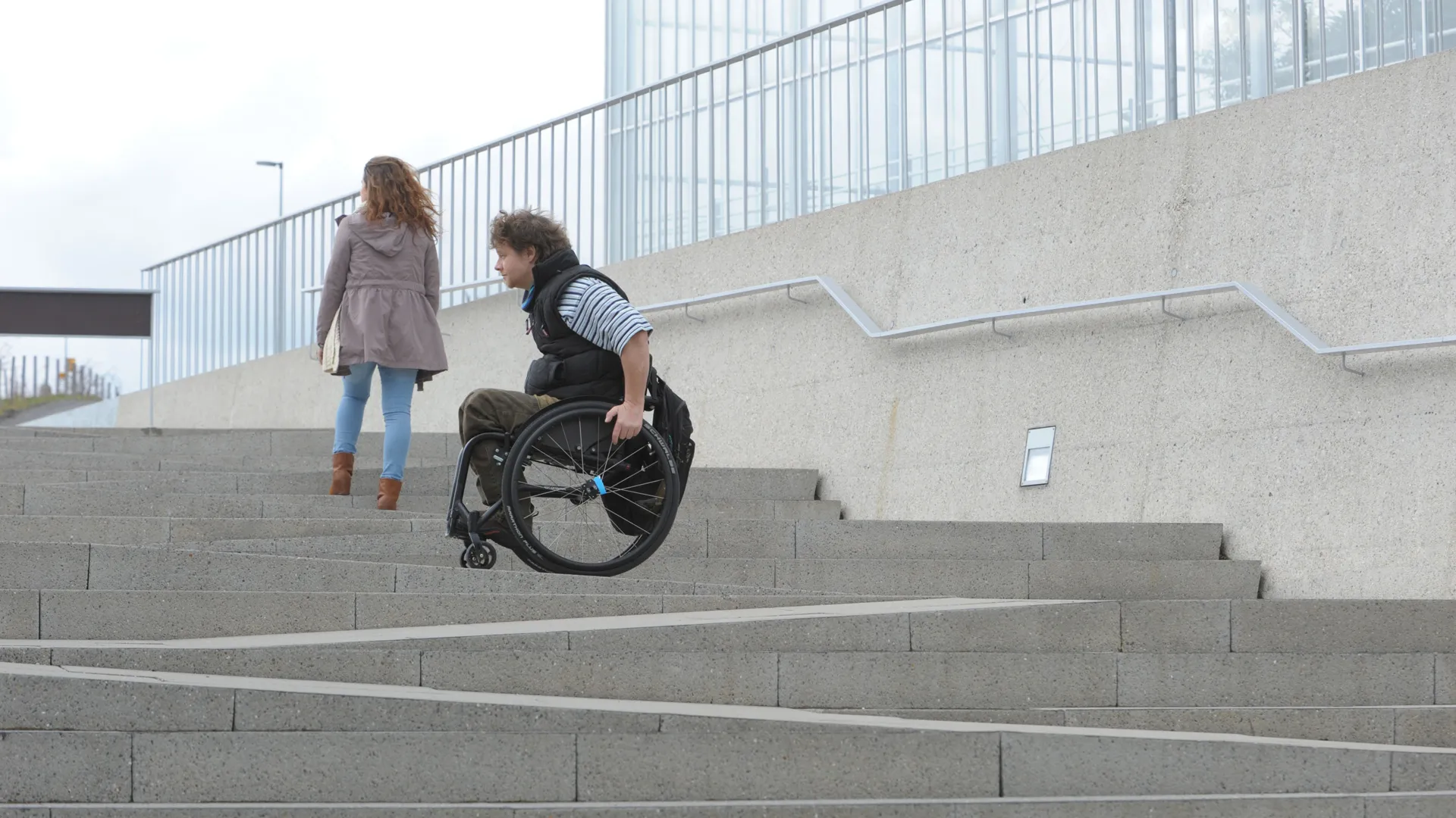 Fussgängerin und Rollstuhlfahrer auf einer Treppe mit Rampe